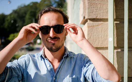 Clément står på ett gathörn i stark sol. Han har kort mörkt hår och ser cool ut i solglasögon och jeansskjorta.