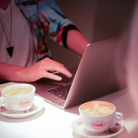 Ett bord med två kaffekoppar och en uppslagen laptop. Två personer skymtar i utkanten av bilden.