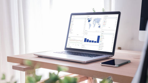 En dator på ett skrivbord. I bakgrunden syns ett fönster med ljusa gardiner.