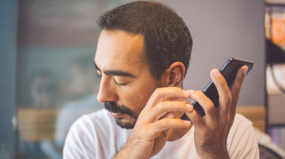 En man håller upp en smartphone en bit från örat. Han blundar och ser ut att lyssna på något.